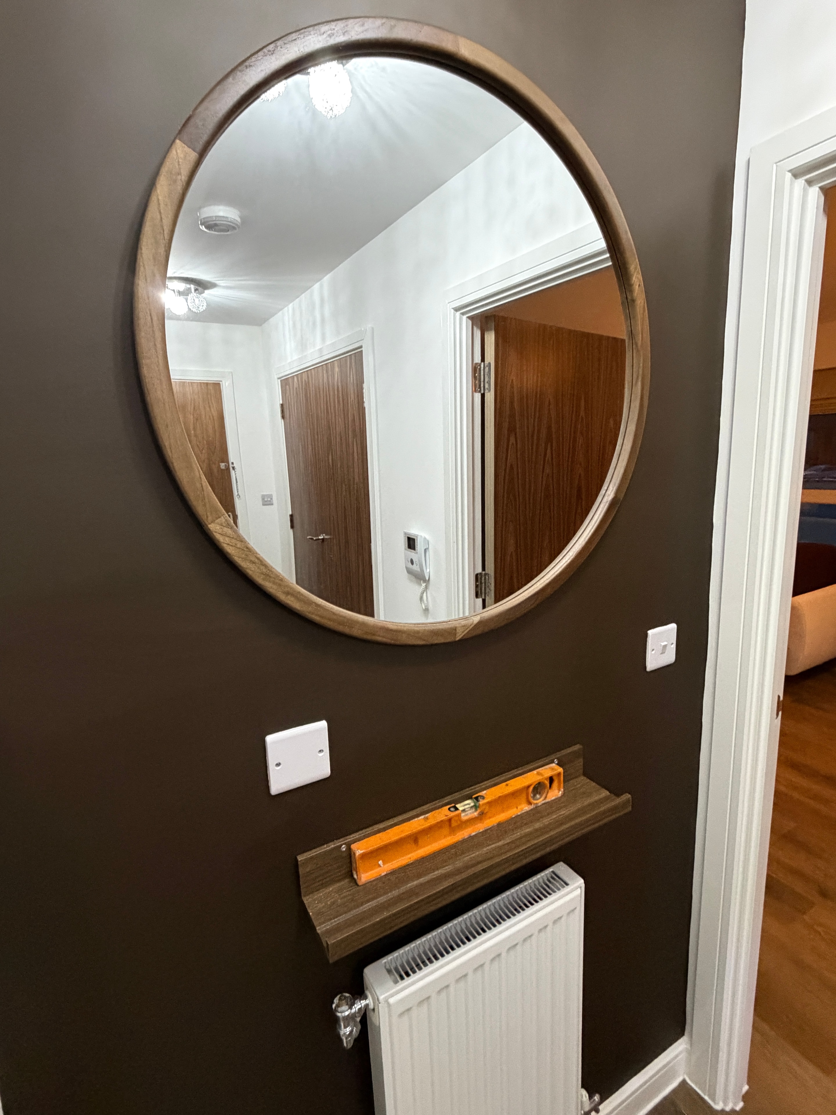 Large round wood-framed mirror mounted on dark feature wall