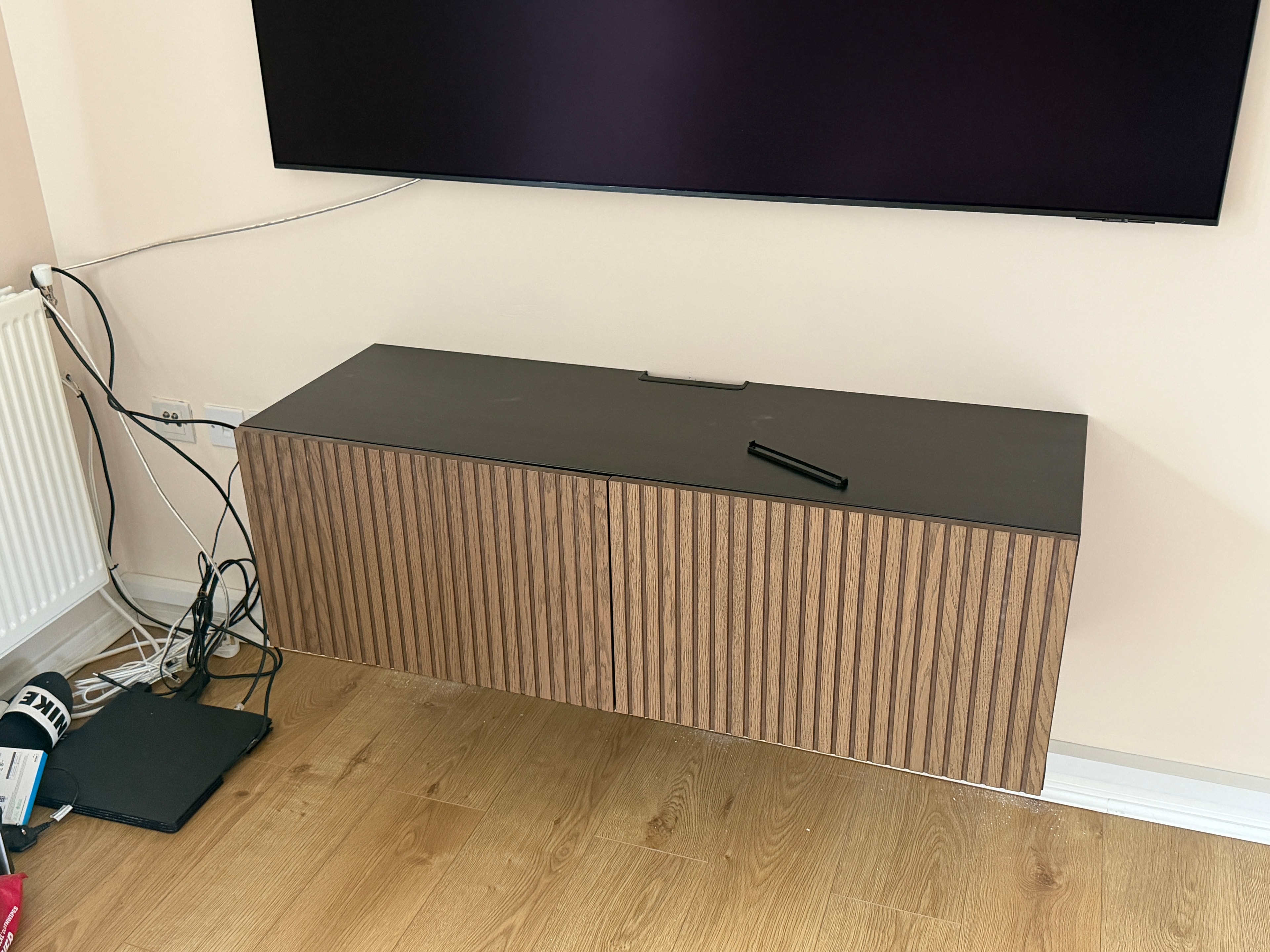 Slatted oak TV unit with black top assembled below wall-mounted TV